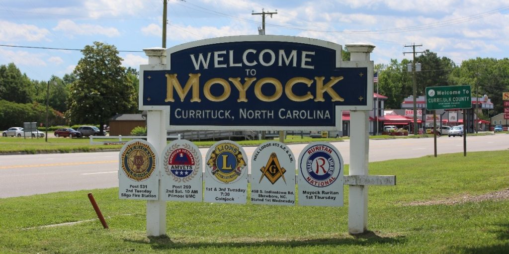 Large street sign displaying "Welcome to Moyock - Currituck, NC" along the highway.